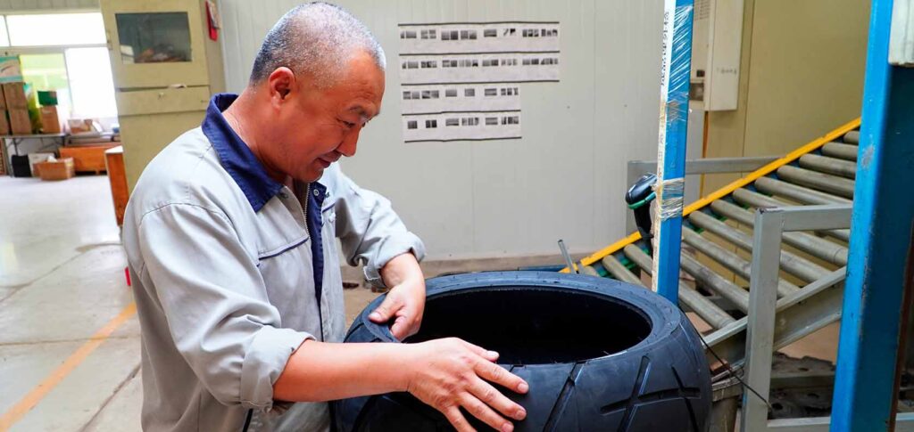 Technician inspecting Kingtyre racing slick motorcycle tire for wear.